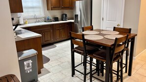 Une cuisine compacte avec des meubles en bois, un réfrigérateur en acier inoxydable, un évier et une table à manger avec quatre chaises.