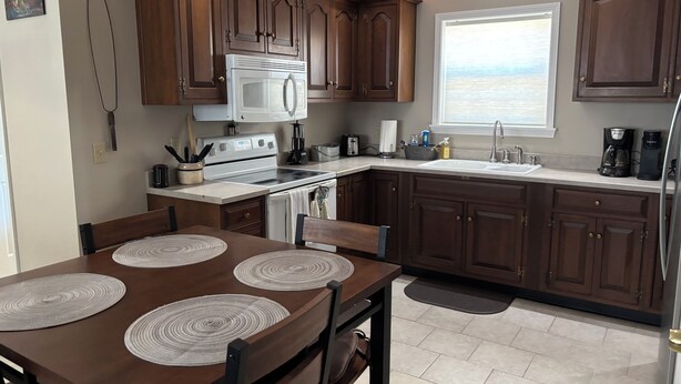Une cuisine moderne avec des meubles en bois foncé, une cuisinière blanche et une grande fenêtre offrant une vue sur l’océan.