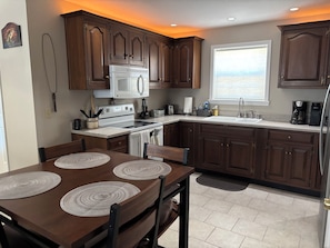 A modern kitchen with dark wooden cabinets, a white stove, and a large window providing a view of the ocean.