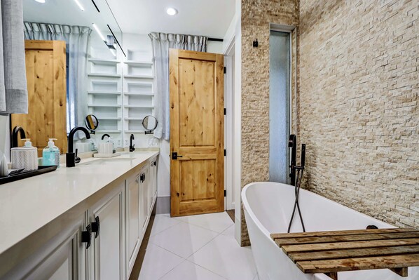 Un baño moderno con una bañera blanca, una puerta de madera y una pared de ladrillo.