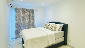 Un dormitorio con cama, ventana con cortinas estampadas y equipo de aire acondicionado.