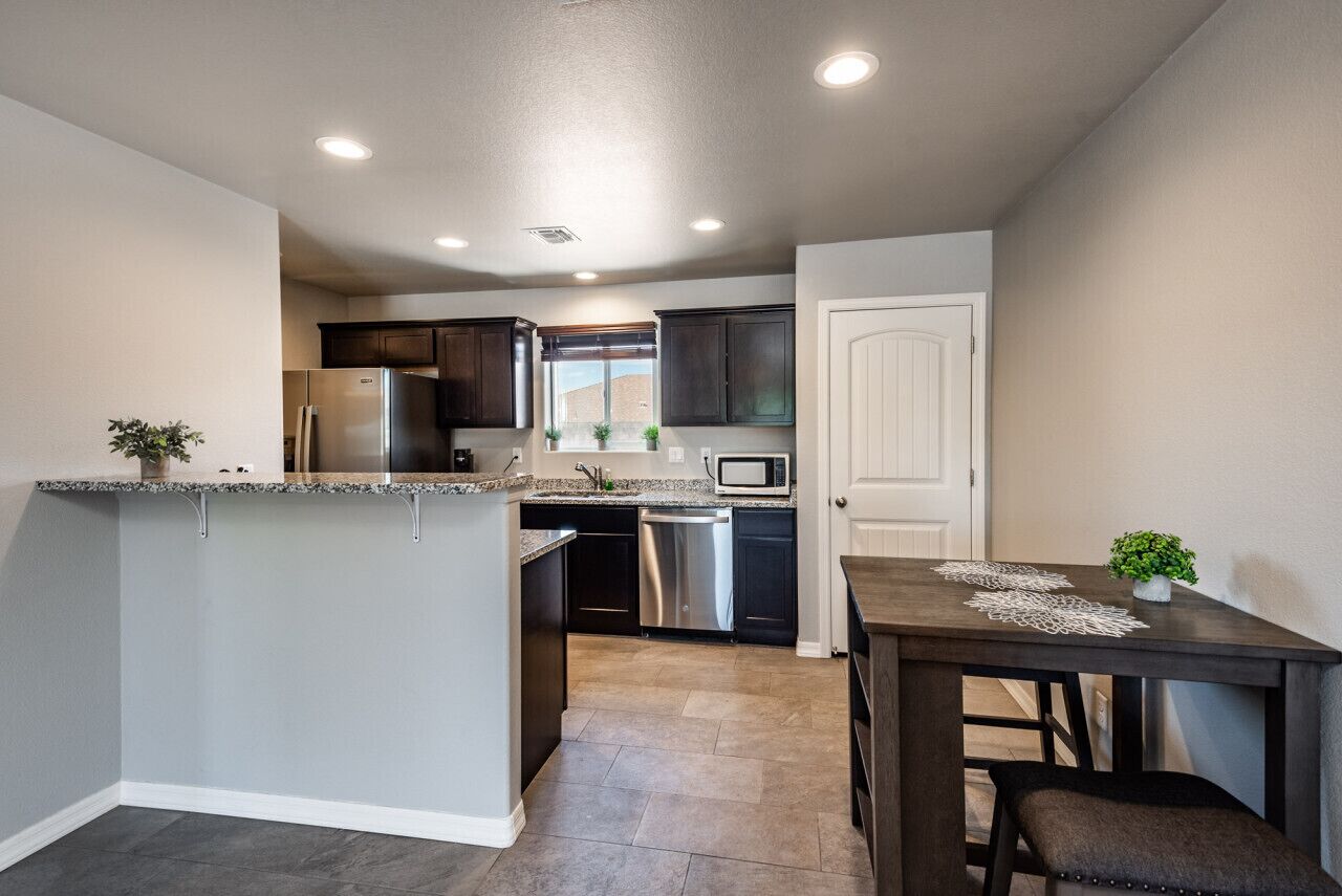 A modern kitchen with granite countertops, stainless steel appliances, and a dining area with a dark wooden table and bench.