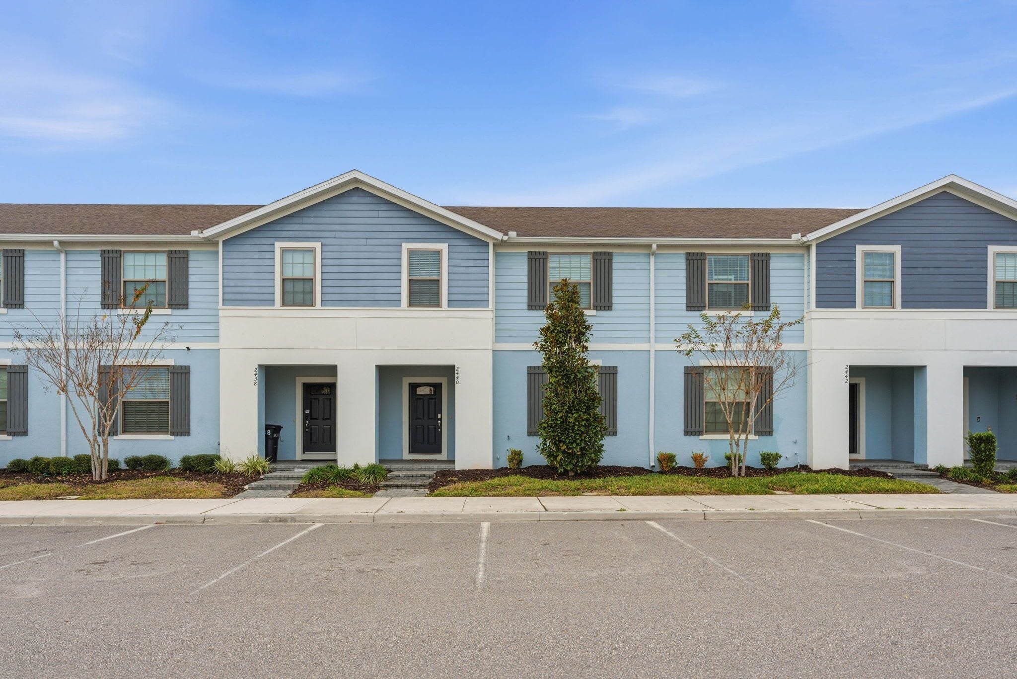 A row of townhouses with a front entrance, a small tree, and a clear sky.