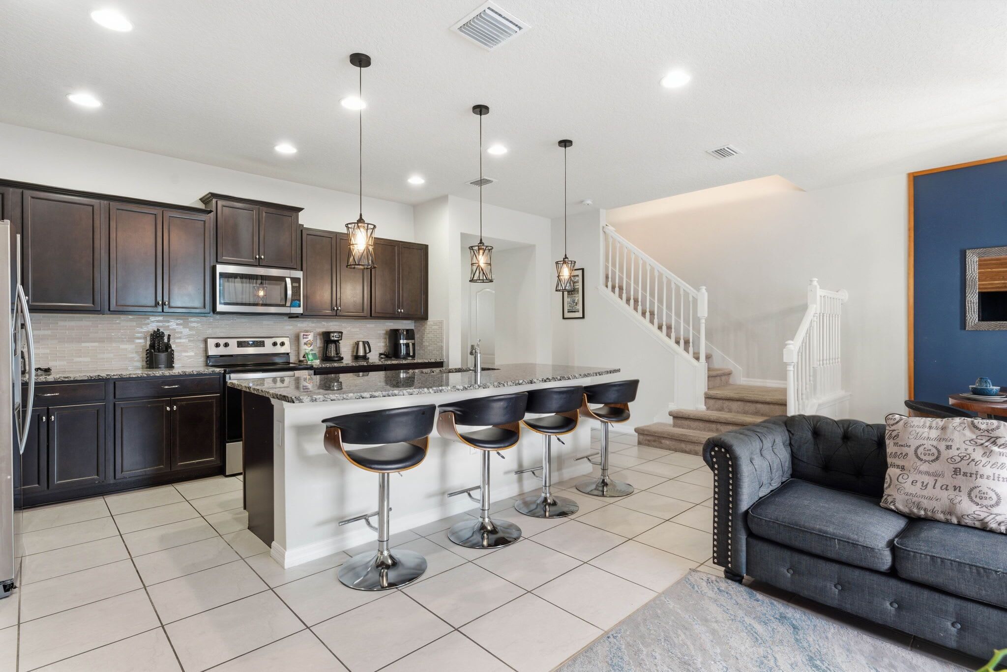 A modern kitchen with dark cabinets, a central island with bar stools, stainless steel appliances, and pendant lighting.