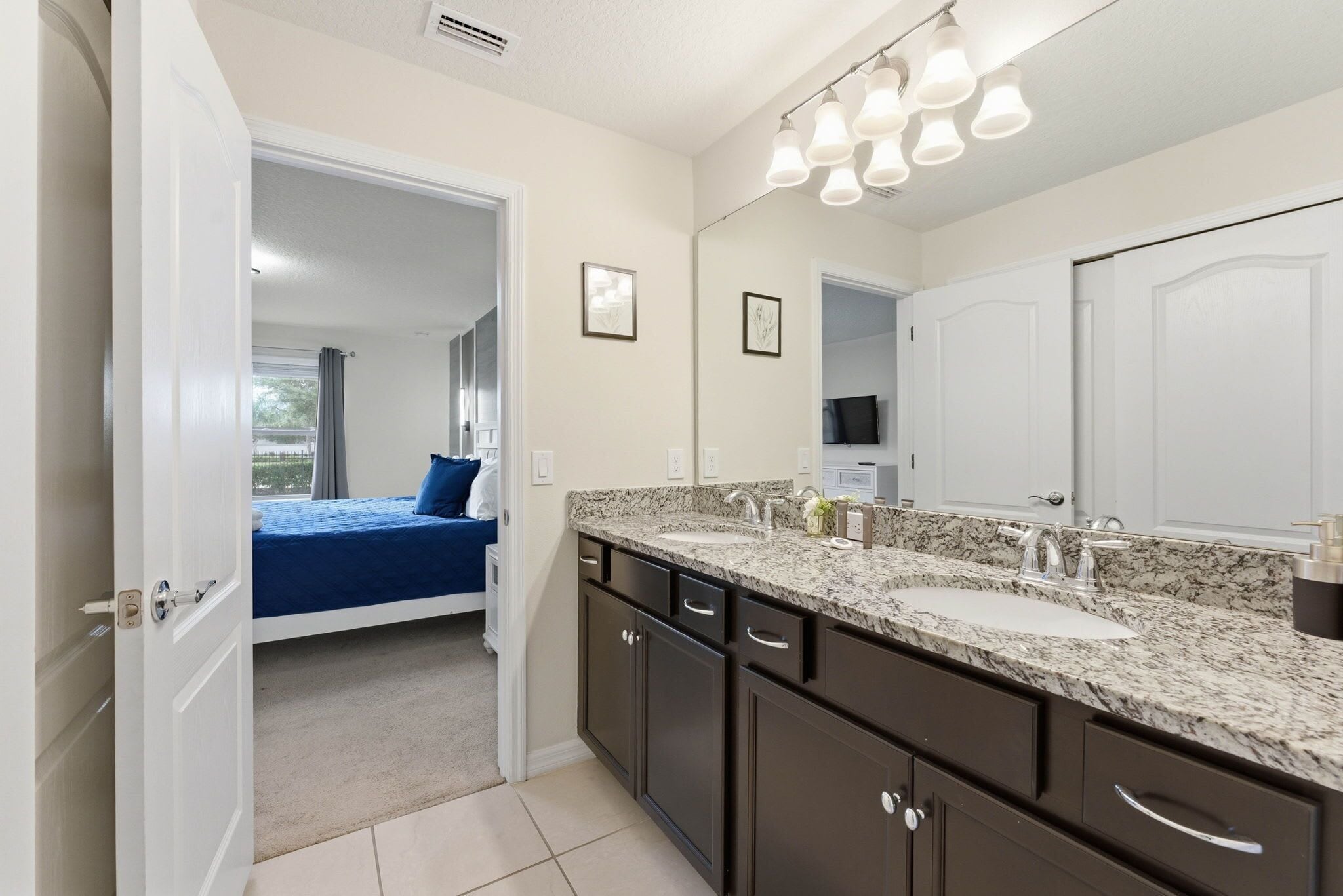 A bathroom with a large mirror, dark cabinets, and a granite countertop.