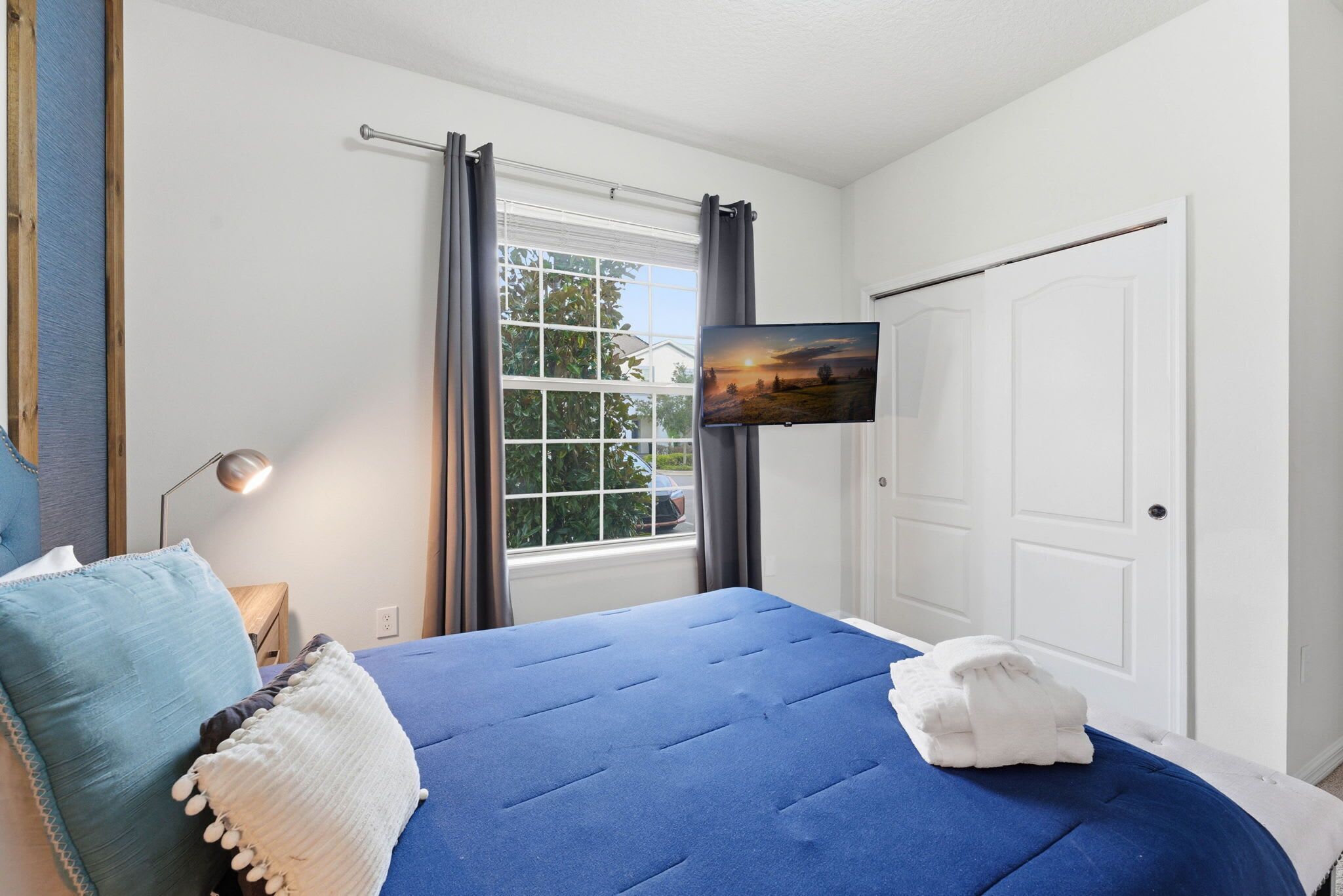 A hotel room with a large bed, a flat-screen TV mounted on the wall, a window with curtains, and a door.