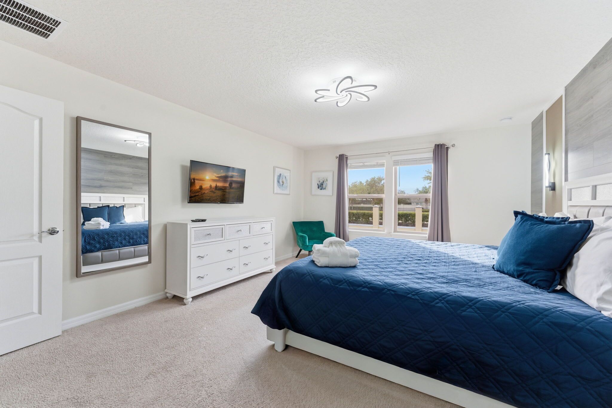 A bedroom with a large bed, a dresser, a chair, and a window with curtains.