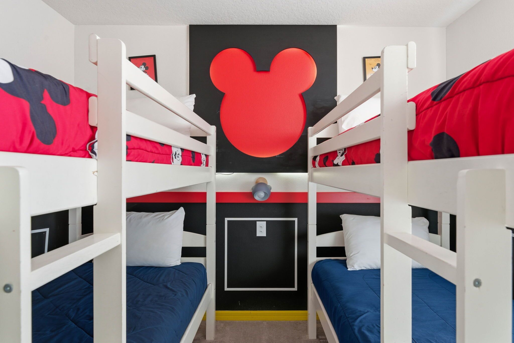 A bunk bed room with a Mickey Mouse cutout on the wall, white railings, and red and blue bedding.
