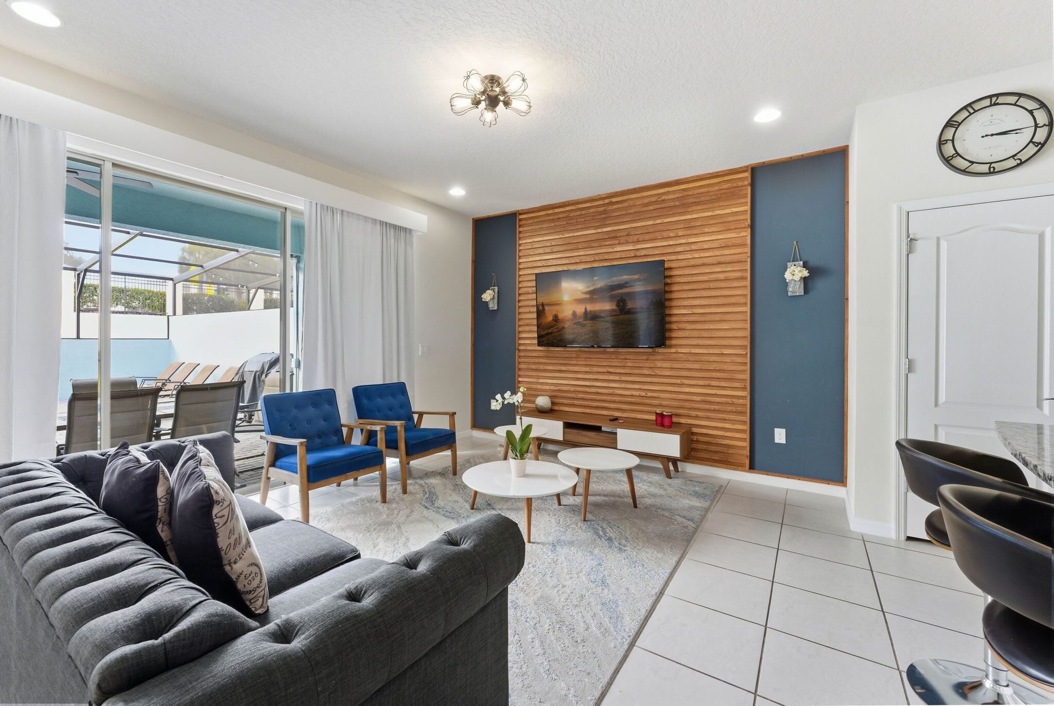 Ein modernes Wohnzimmer mit einem grauen Sofa, blauen Sesseln, einem Couchtisch und einem an einer Holzvertäfelung montierten Fernseher.