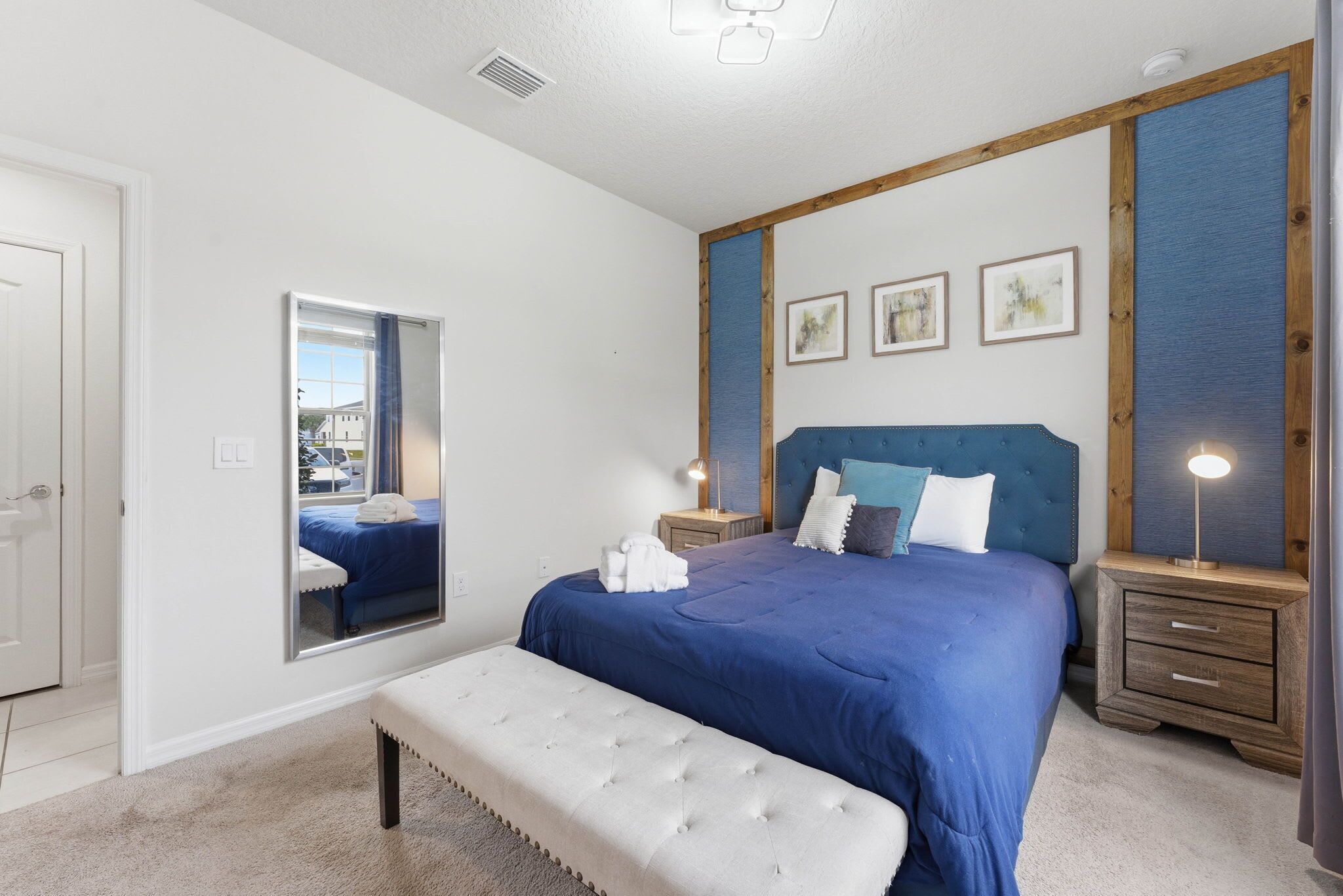 A bedroom with a large bed, a mirror, a bedside table with a lamp, and a wooden headboard.