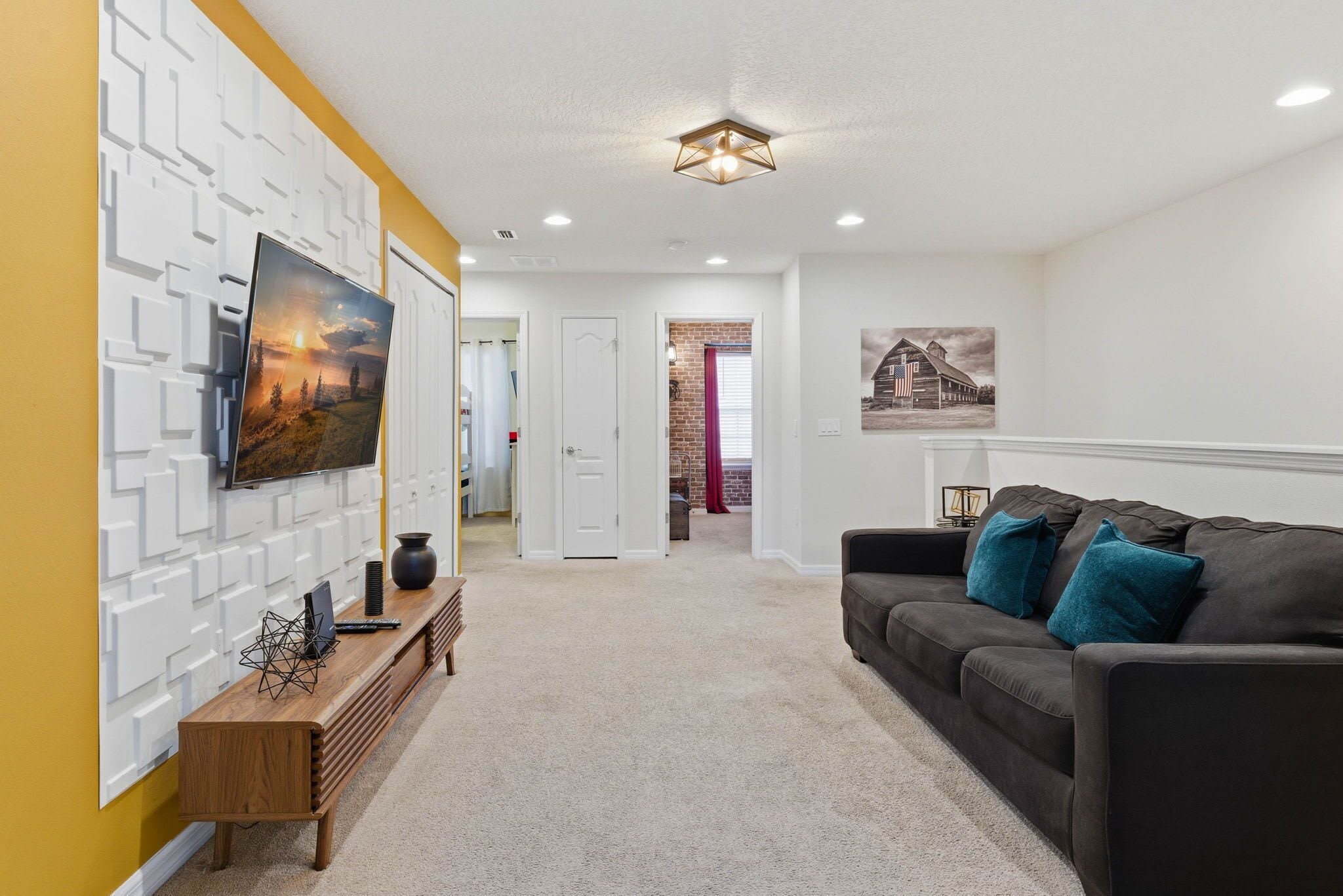 A modern living room with a sectional sofa, a flat-screen TV mounted on a white wall, and a decorative wall panel.