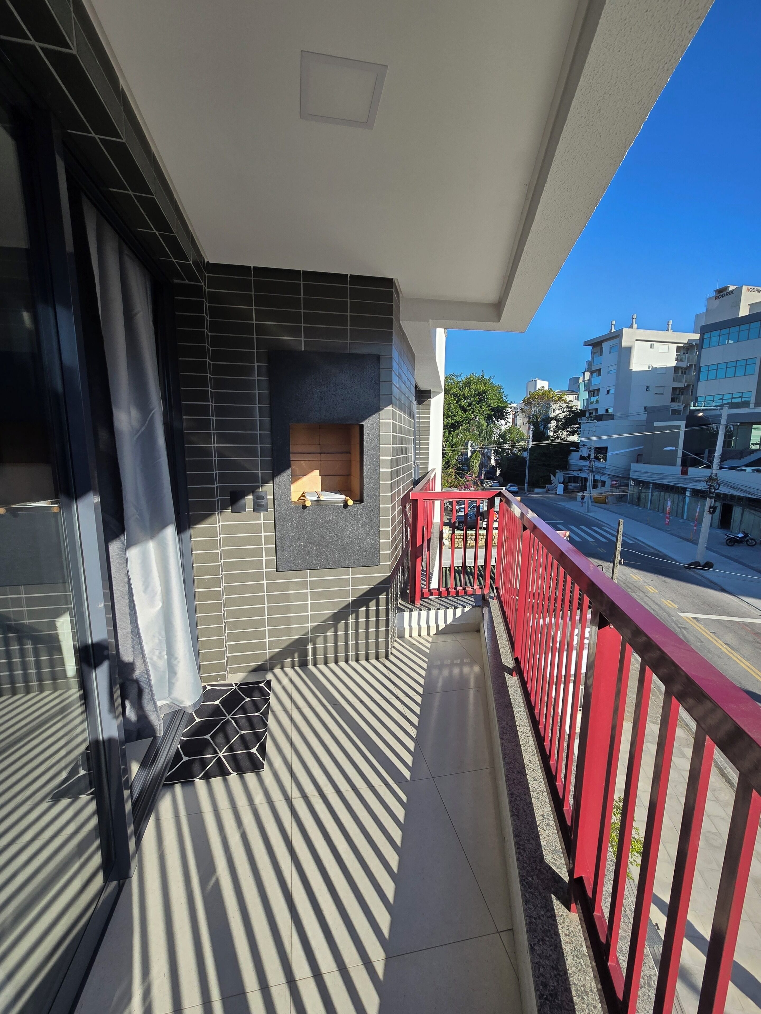 A balcony with a tiled floor, a red railing, and a view of the street and buildings.