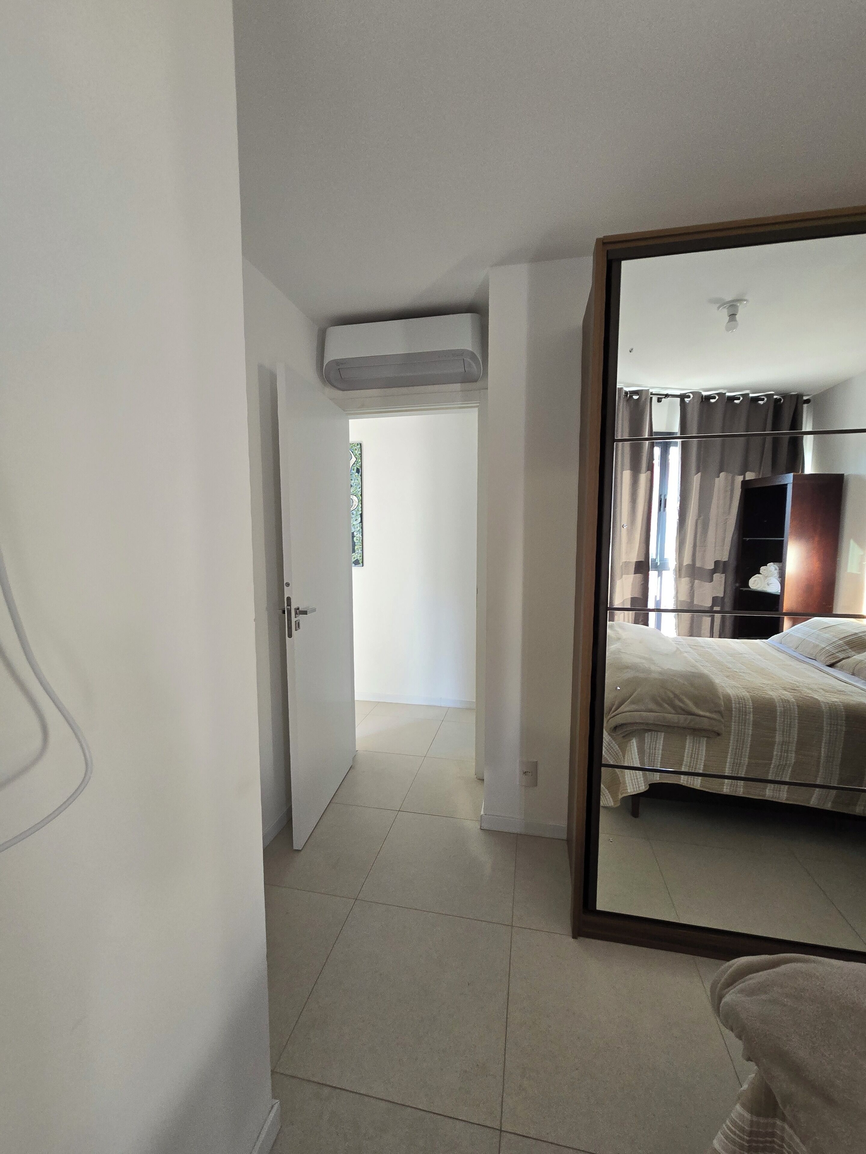 A bedroom with a bed, a mirror, and a door leading to another room.