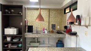A modern kitchen with granite countertops, a built-in microwave, a sink, and a gas stove. There are hanging pendant lights and a shelf with kitchen items. - Flat Gold Vista Mar - Praia de Tabatinga (Conde)