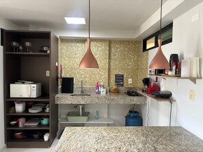 A modern kitchen with granite countertops, a built-in microwave, a sink, and a gas stove. There are hanging pendant lights and a shelf with kitchen items. - Flat Gold Vista Mar - Praia de Tabatinga (Conde)