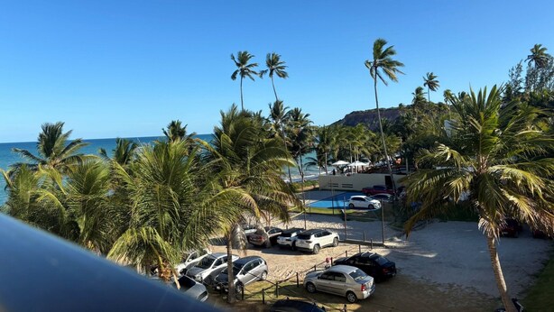 A beachside parking area with cars, palm trees, and a pool. - Flat Gold Vista Mar - Praia de Tabatinga (Conde)