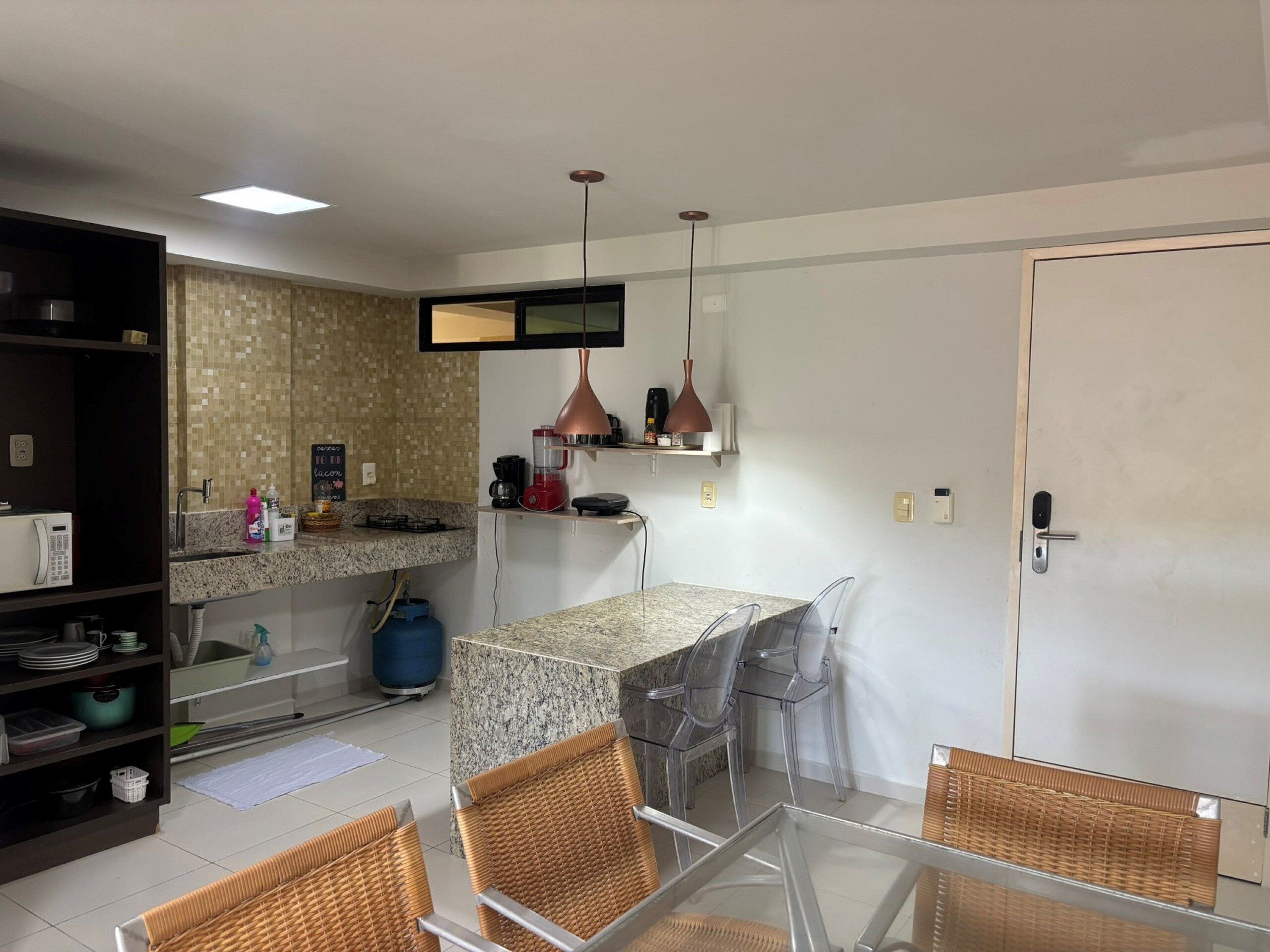 Cocina moderna con encimera de granito, horno empotrado, cafetera y hervidor rojo. Hay sillas de mimbre y una mesa de vidrio.