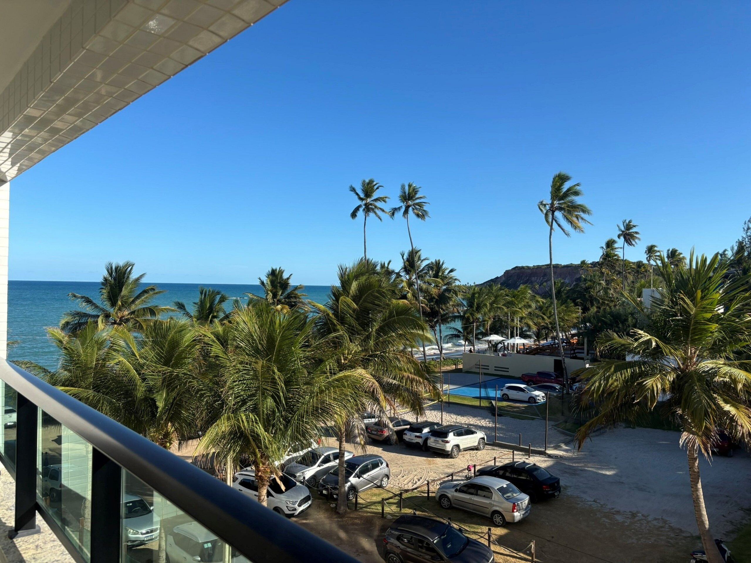 Ein Parkplatz direkt am Strand mit Autos, Palmen und freiem Blick auf den Ozean.