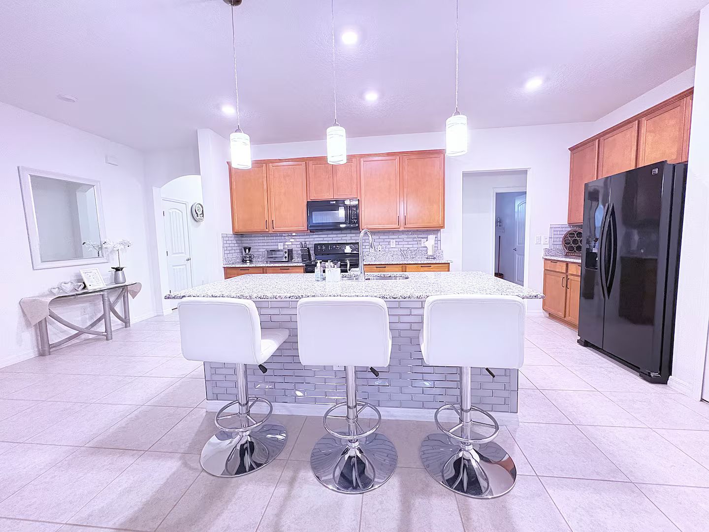 Una cocina moderna con una isla central, taburetes de bar, armarios de madera y un refrigerador negro.