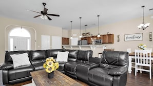 A modern living room with a sectional sofa, a wooden coffee table, and a kitchen in the background. - Game Room - Wind Creek Casino- RTJ Golf - 3 Beds - 2 Bath (Wetumpka)