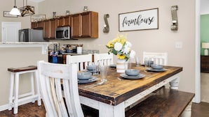 A dining area with a wooden table set for four, white chairs, and a vase of flowers. - Game Room - Wind Creek Casino- RTJ Golf - 3 Beds - 2 Bath (Wetumpka)