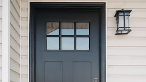 A dark brown front door with a glass panel, a keypad lock, and a doormat with the text "so happy you're here." - Spacious 6BR 3BA • Sleeps 16 • Across from Large Park (West Jordan)