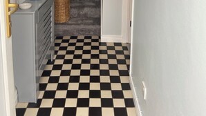 A hallway with a checkered floor, a staircase, a small cabinet with a mirror, and a 'BEACH' sign on the wall.
