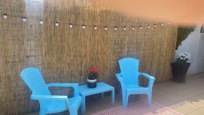 A seating area with two blue chairs and a small table, a patterned rug, and a wall decorated with vertical bamboo strips and string lights.