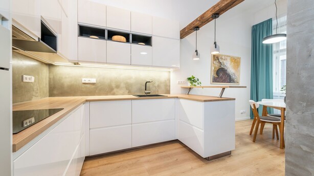 Een moderne keuken met witte kasten, een houten aanrechtblad en een ingebouwd spoelbakje. Er is een eethoek met een tafel en stoelen, en een schilderij aan de muur.