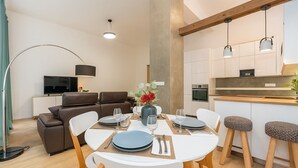 Een moderne woonkamer met een eethoek, een bank, een televisie en een keuken met een houten aanrechtblad en hangende lampen.
