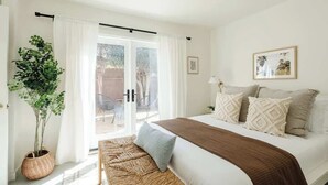 Ein Schlafzimmer mit einem Bett, einer Sitzbank, einem Topf mit Pflanze und einer Schiebetür zu einem Außenbereich.