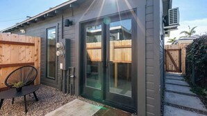 Ein modernes Haus mit Schiebeglastür, einer kleinen Terrasse mit Stuhl und Pflanze sowie einem Holzzaun.