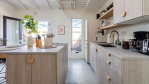 A modern kitchen with wooden cabinets, a central island, and a view to the outside. - Unique & Cozy Gem: Mins to Beach ~ Patio (San Diego)