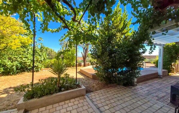 A covered patio area with a wooden deck, surrounded by various plants and trees. - Gorgeous home in Villespassans (VILLESPASSANS)