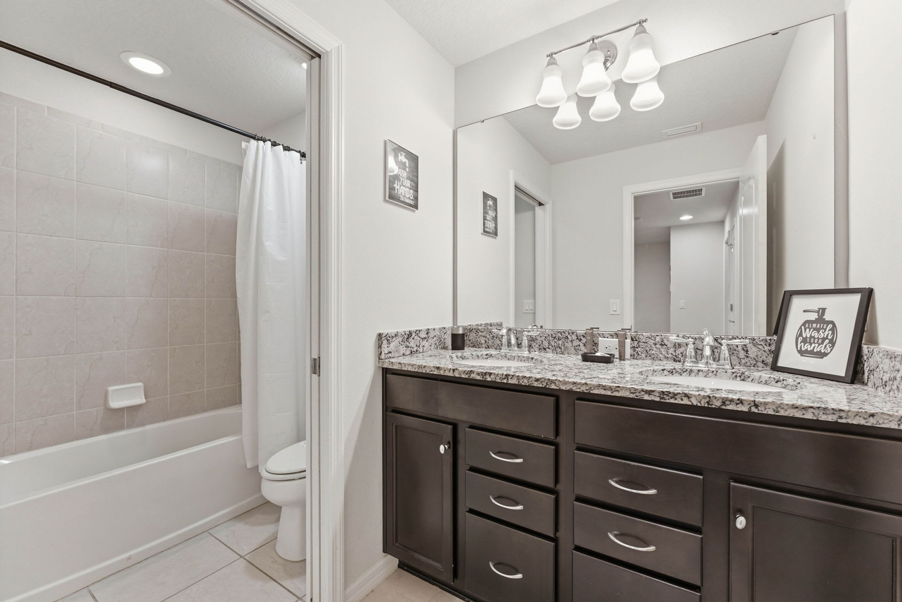 A modern bathroom with a shower, toilet, and vanity with a large mirror and multiple drawers.