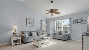 Un salon avec deux canapés gris, une table basse blanche, un ventilateur de plafond et un vélo accroché au mur.