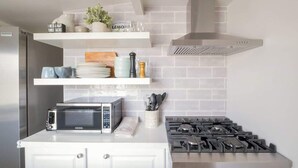 Una cocina con microondas, estufa y repisas con utensilios de cocina.