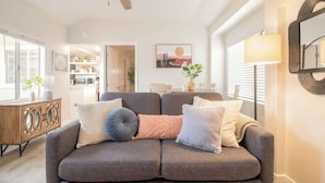 Una sala de estar con un sofá gris, un mueble de madera, un ventilador de techo y una ventana con persianas.