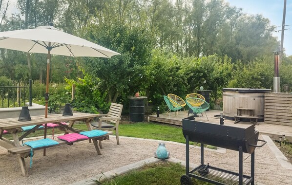 A patio with a wooden table and chairs, a barbecue grill, and a large umbrella. - Gite Bain nordique et rivière (CLAIRMARAIS)
