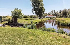 A serene outdoor setting with a pond, lush greenery, and a building with a red roof. - Gite Bain nordique et rivière (CLAIRMARAIS)