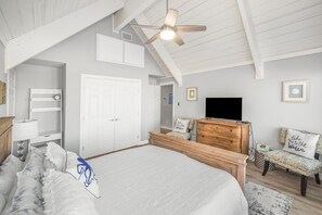 Ein Schlafzimmer mit einem großen Bett, einer hölzernen Kommode, einem Fernseher und einem Deckenventilator.