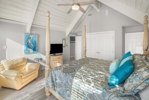 Ein Schlafzimmer mit Bett, Fernseher, Kommode, Sofa und Deckenventilator.