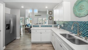 Una cocina moderna con armarios blancos, electrodomésticos de acero inoxidable y un salpicadero de mosaico azul.