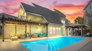 Una casa de dos plantas con piscina, zona de estar exterior y un porche cubierto.