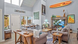 Amplia sala de estar con techo alto, zona de comedor y decoración temática de playa, incluyendo una tabla de surf y un letrero que dice "BEACH HOUSE".