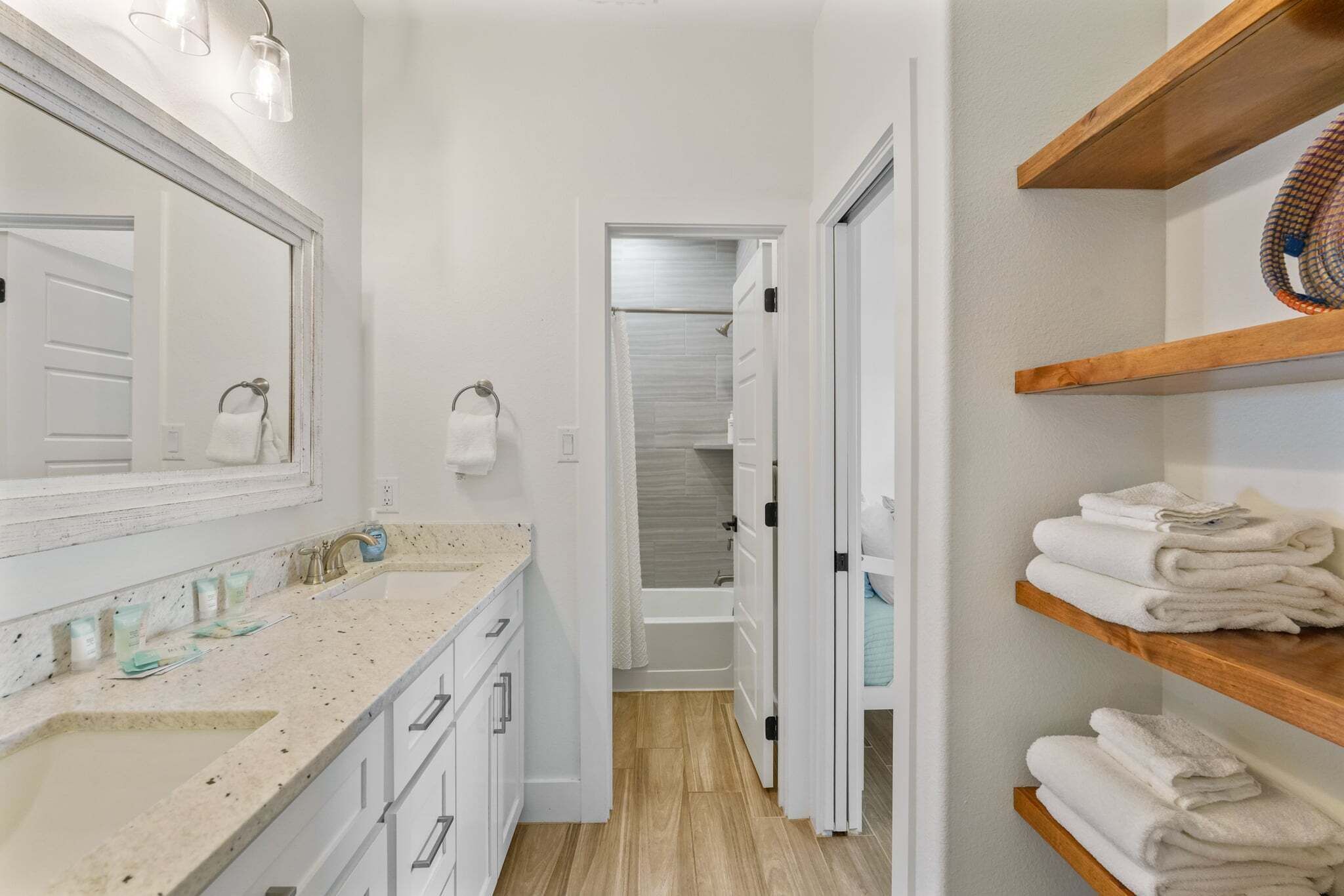 Un baño con lavabo, espejo, toallero y estantes de madera con toallas dobladas.