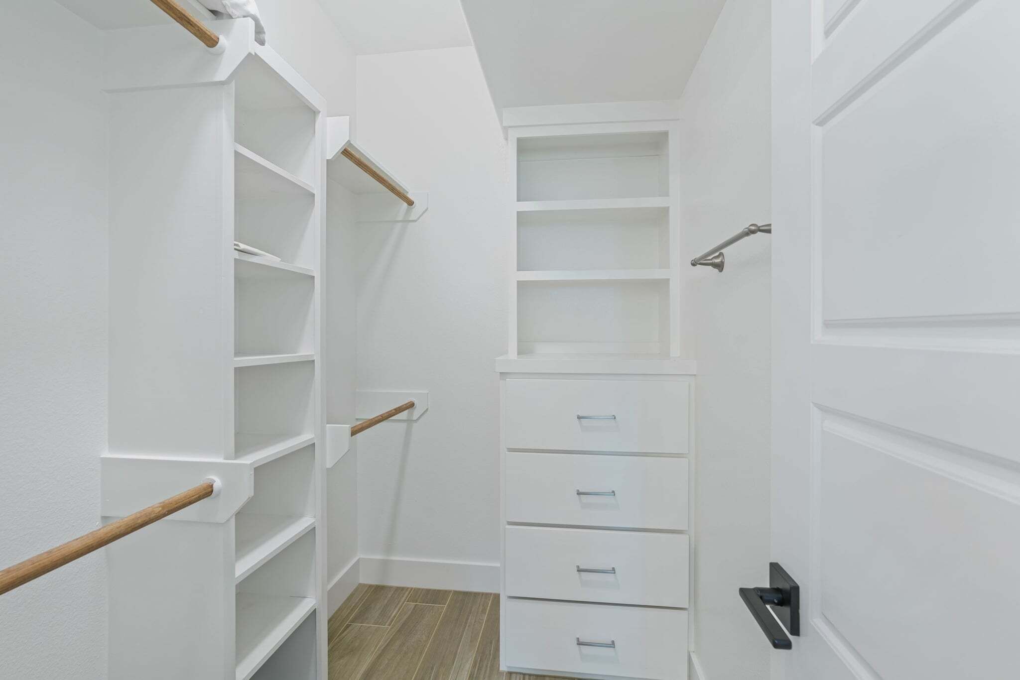 A narrow walk-in closet with white shelving, drawers, and a wooden coat rack.