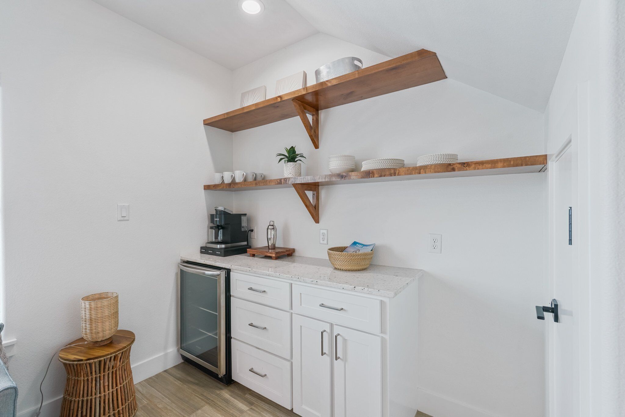 A compact kitchen with white cabinets, a coffee machine, and wooden shelves above.