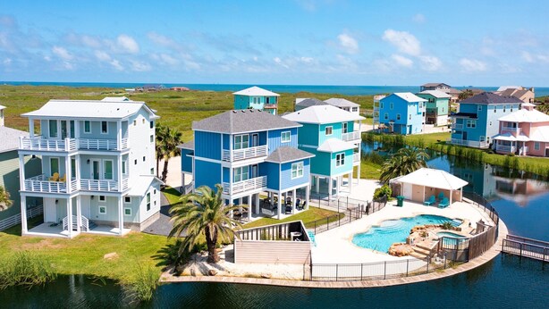 Ett bostadsområde vid kusten med flera tvåvåningshus, en swimmingpool och en brygga.