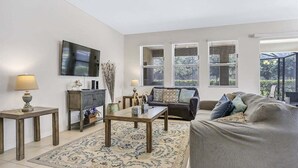 A living room with a sofa, a coffee table, a TV, and a window with blinds. - 6079-7-bo-enchanted Villa by Disney (Davenport)